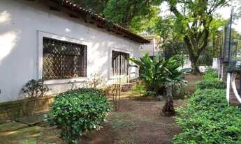 Imagem 3: Casarão antigo de esquina, com amplo jardim e gramado em volta da casa, com árvores frutíf